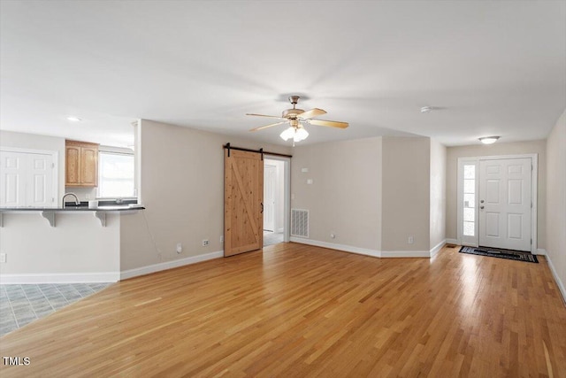 unfurnished living room featuring light wood finished floors, a barn door, visible vents, baseboards, and ceiling fan