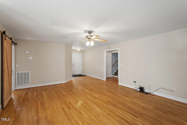 unfurnished room with a barn door, light wood-style flooring, visible vents, and baseboards