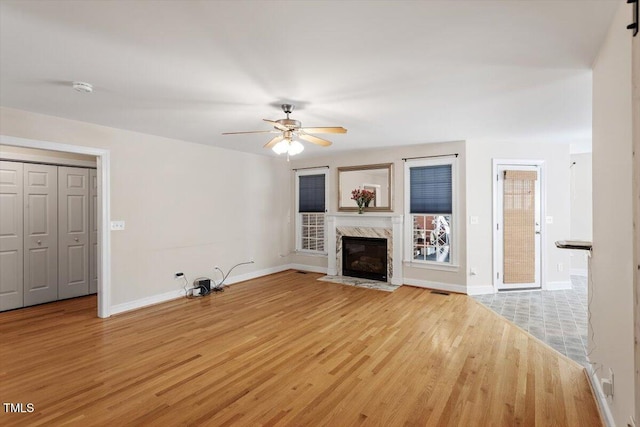 unfurnished living room with light wood finished floors, ceiling fan, a premium fireplace, and baseboards