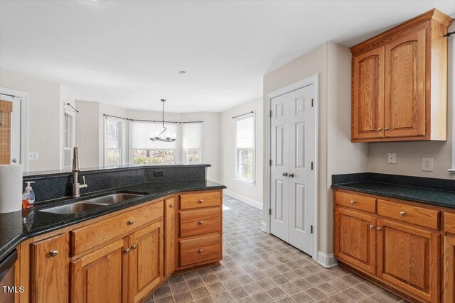 kitchen with dark stone counters, hanging light fixtures, brown cabinetry, and a sink