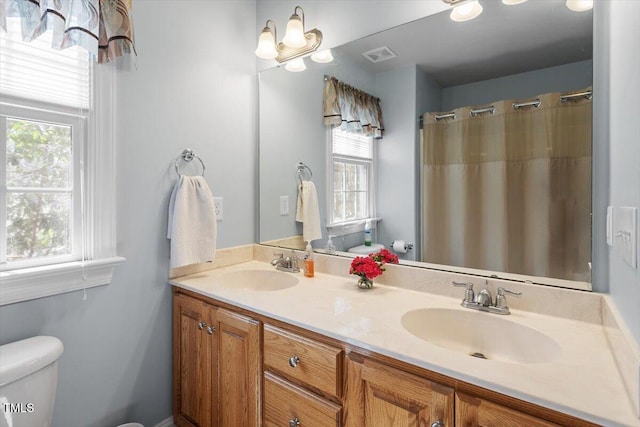 full bath with visible vents, a sink, toilet, and double vanity