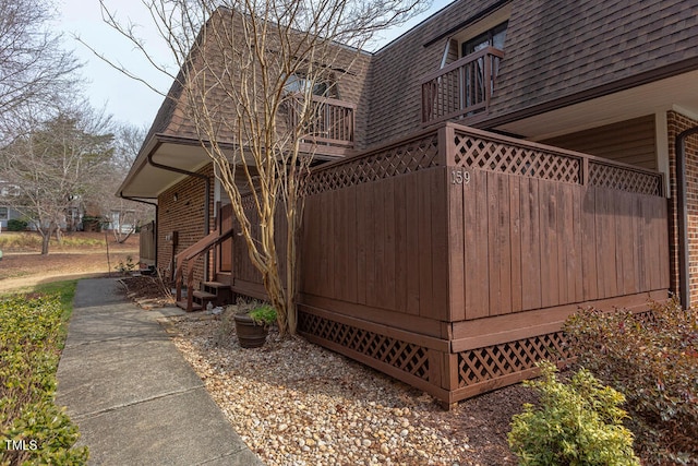 view of side of property with entry steps, roof with shingles, brick siding, and mansard roof