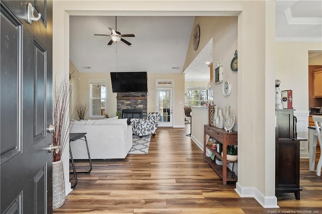 living room with light wood-type flooring, ceiling fan, a stone fireplace, and baseboards