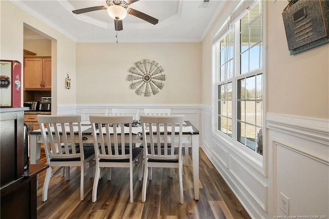 dining room with a raised ceiling, a wainscoted wall, ornamental molding, dark wood-type flooring, and a decorative wall