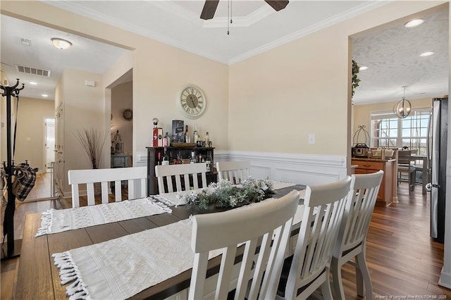 dining room with a wainscoted wall, wood finished floors, visible vents, and crown molding