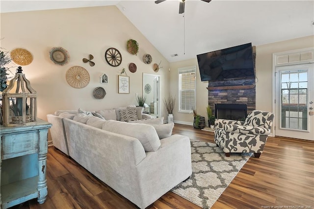 living area featuring high vaulted ceiling, dark wood-style flooring, a stone fireplace, and a ceiling fan