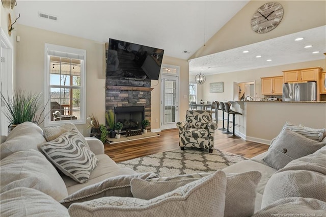 living room with a stone fireplace, wood finished floors, visible vents, and recessed lighting