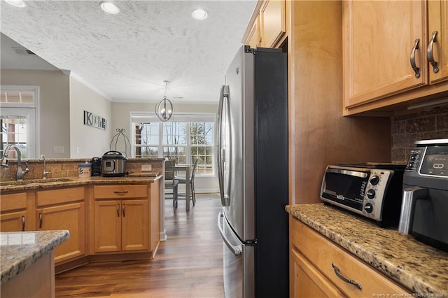 kitchen featuring dark wood finished floors, decorative backsplash, freestanding refrigerator, a sink, and light stone countertops