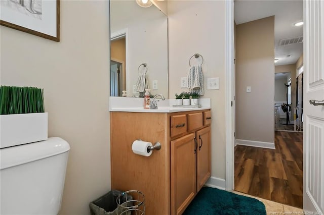 half bath with toilet, wood finished floors, vanity, visible vents, and baseboards