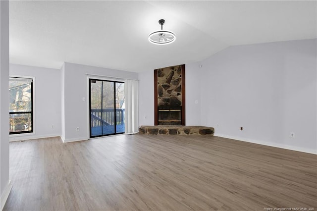 unfurnished living room with lofted ceiling, a fireplace, baseboards, and wood finished floors