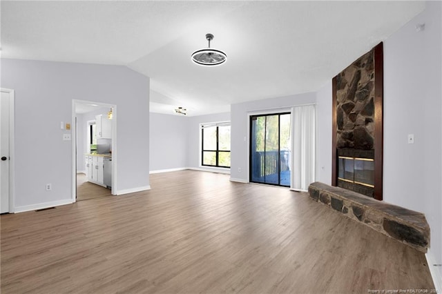 living room featuring vaulted ceiling, a fireplace, baseboards, and wood finished floors