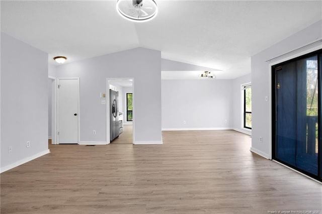 spare room with light wood-style floors, vaulted ceiling, and baseboards