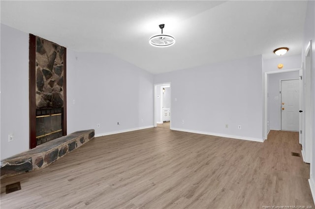 unfurnished living room featuring vaulted ceiling, a stone fireplace, baseboards, and wood finished floors