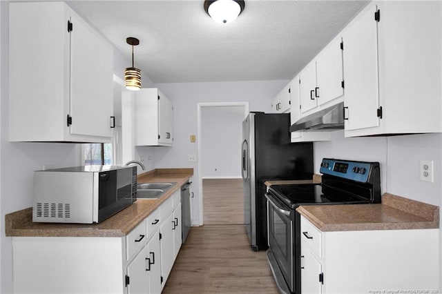 kitchen featuring light wood finished floors, stainless steel appliances, white cabinets, a sink, and under cabinet range hood