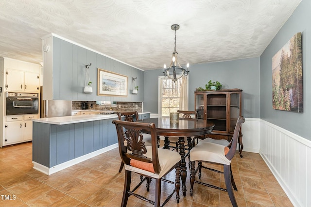 dining area with a wainscoted wall, a textured ceiling, and an inviting chandelier