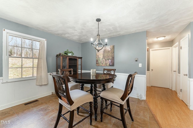 dining area with a textured ceiling, wainscoting, a chandelier, and visible vents