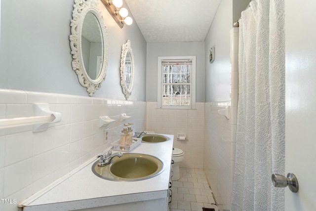 full bath with a wainscoted wall, a sink, toilet, and tile patterned floors