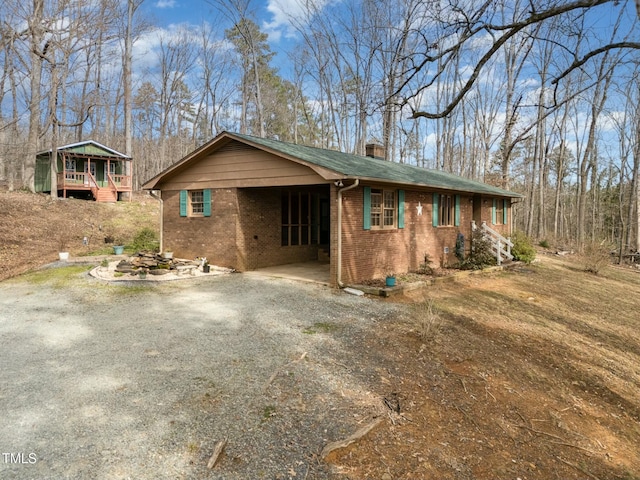 view of front of house featuring gravel driveway, brick siding, and a chimney