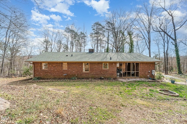 rear view of house with a sunroom, brick siding, a yard, and a chimney