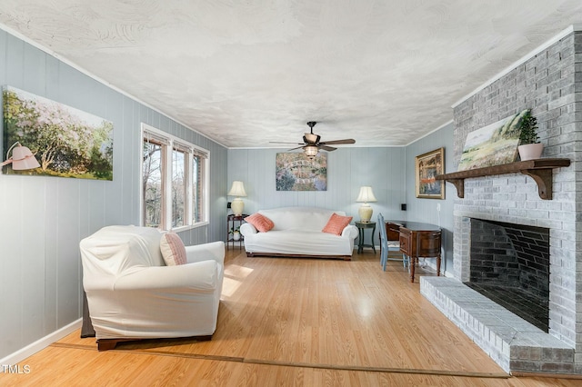 living area with a brick fireplace, baseboards, a ceiling fan, and wood finished floors