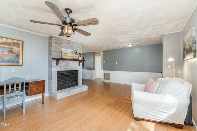 living room featuring light wood finished floors, visible vents, a ceiling fan, a textured ceiling, and a brick fireplace