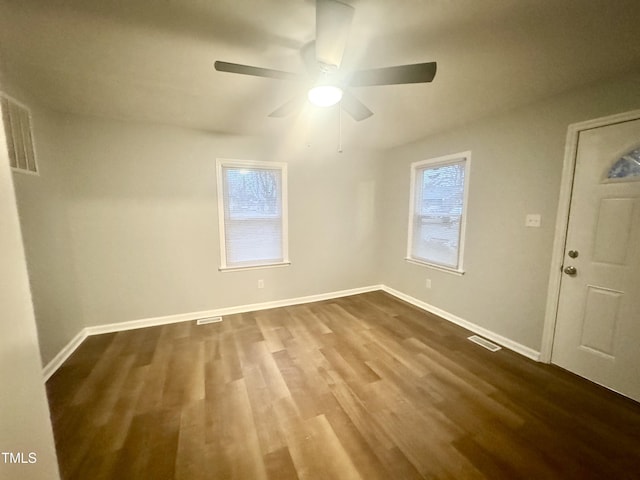 spare room with dark wood-style floors, visible vents, ceiling fan, and baseboards