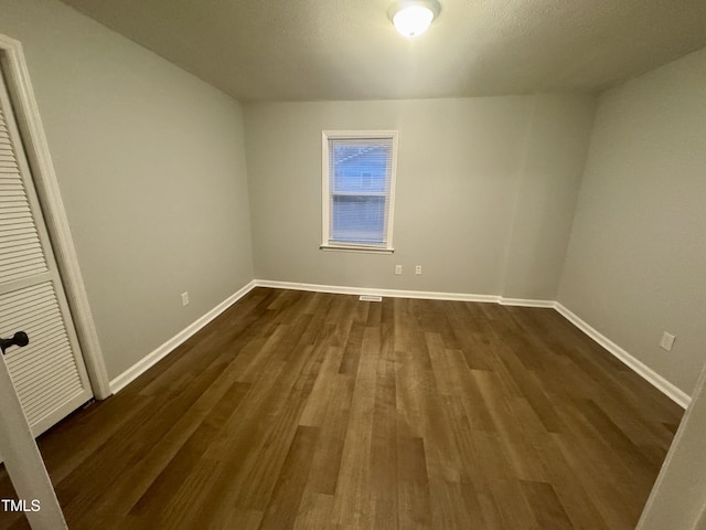 unfurnished bedroom featuring dark wood-type flooring, a closet, and baseboards