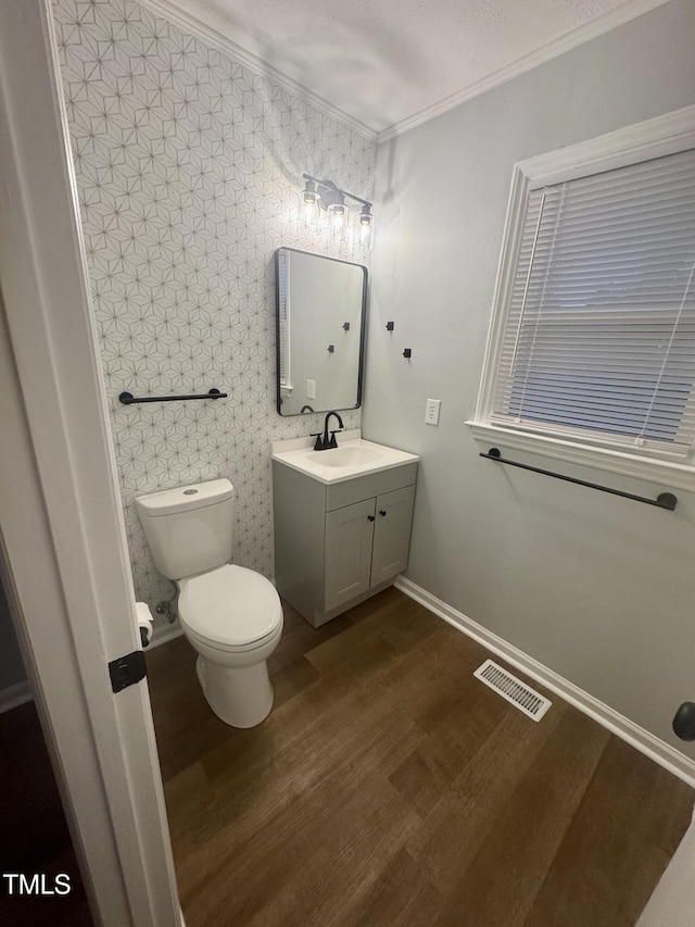 half bathroom featuring visible vents, toilet, wood finished floors, crown molding, and vanity