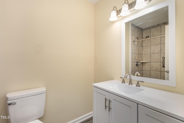 bathroom featuring toilet, baseboards, a tile shower, and vanity