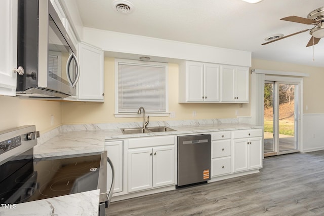 kitchen with light stone counters, stainless steel appliances, visible vents, a sink, and light wood-type flooring