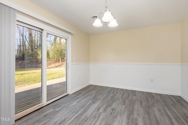 empty room with a chandelier, wood finished floors, and wainscoting