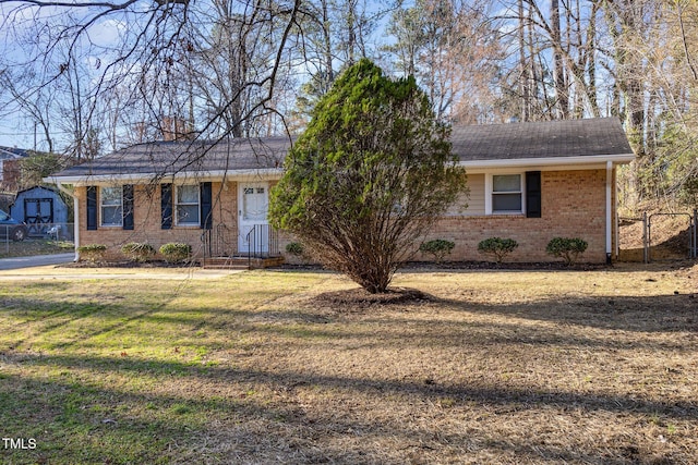 ranch-style home with brick siding, a shingled roof, a chimney, fence, and a front yard