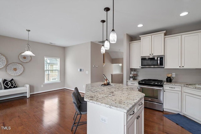 kitchen with light stone countertops, a kitchen island, dark wood finished floors, stainless steel appliances, and white cabinetry