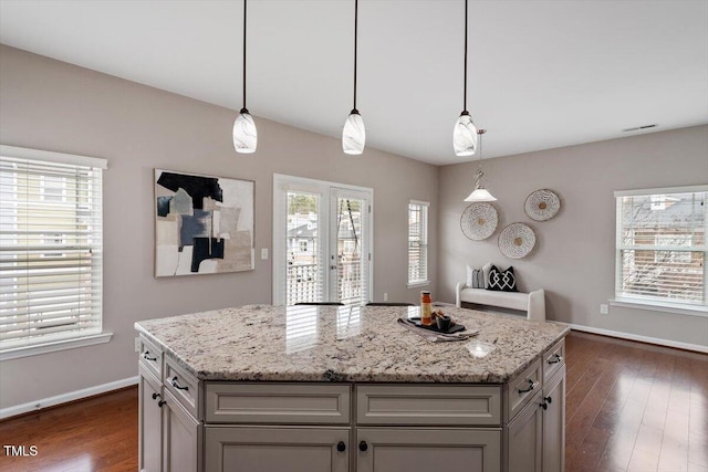 kitchen with visible vents, a kitchen island, baseboards, light stone countertops, and dark wood finished floors