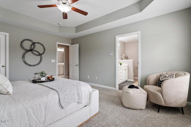 carpeted bedroom featuring a tray ceiling, baseboards, and ensuite bathroom