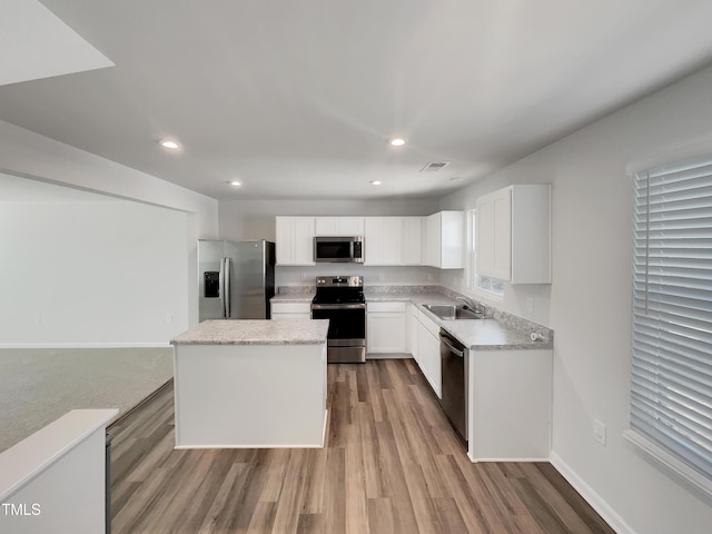 kitchen featuring stainless steel appliances, a kitchen island, a sink, visible vents, and white cabinetry