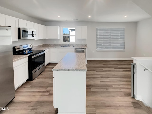 kitchen with appliances with stainless steel finishes, a kitchen island, white cabinetry, and light wood-style floors