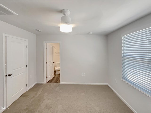 unfurnished bedroom featuring light carpet, ensuite bathroom, visible vents, and baseboards