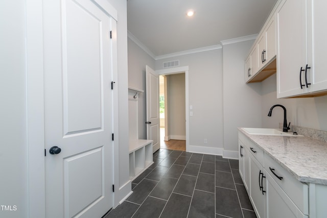 kitchen featuring a sink, white cabinetry, visible vents, baseboards, and ornamental molding