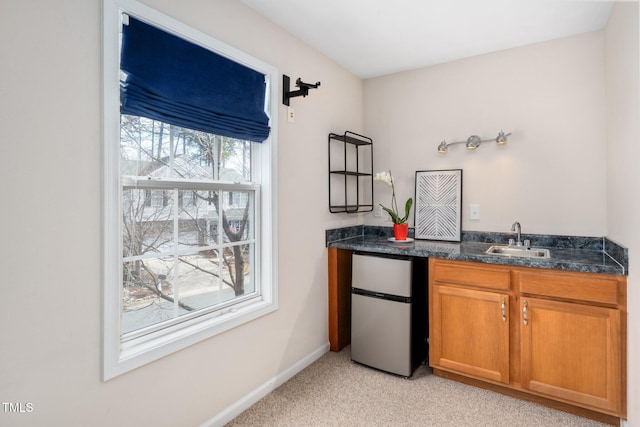 bar featuring light carpet, a sink, freestanding refrigerator, and baseboards