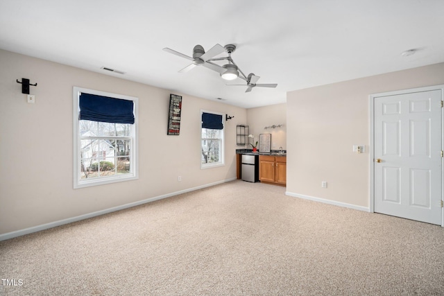 interior space featuring ceiling fan, baseboards, visible vents, and light colored carpet