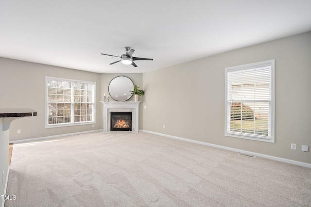 unfurnished living room with carpet floors, a healthy amount of sunlight, a premium fireplace, and baseboards