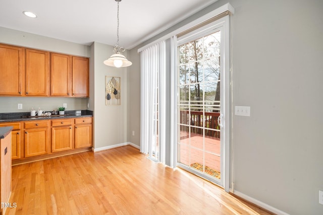 kitchen with baseboards, brown cabinetry, dark countertops, light wood-type flooring, and pendant lighting