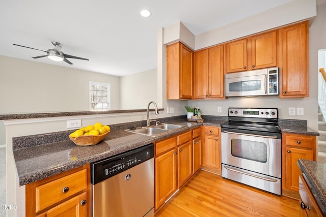 kitchen featuring light wood-style flooring, a sink, appliances with stainless steel finishes, brown cabinets, and dark stone countertops