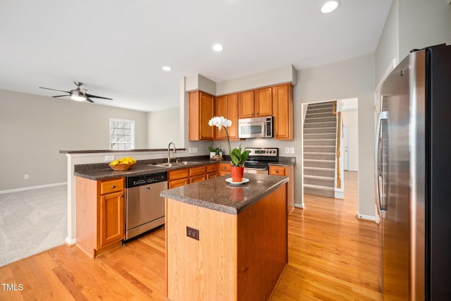 kitchen with stainless steel appliances, a peninsula, a sink, light wood-type flooring, and a center island