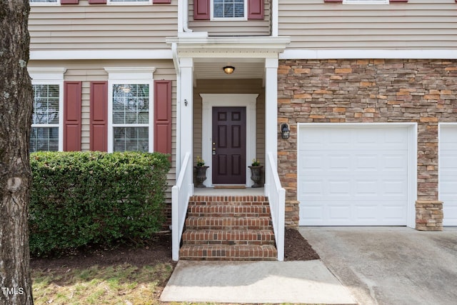 property entrance with a garage, stone siding, and driveway