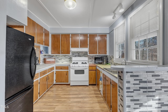 kitchen featuring a sink, light countertops, freestanding refrigerator, brown cabinetry, and white gas range