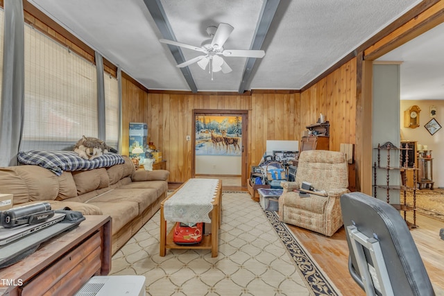 living room featuring ceiling fan, light wood finished floors, beam ceiling, and wooden walls