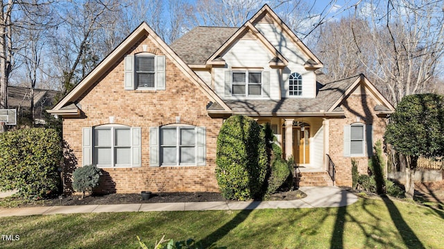 view of front of home featuring roof with shingles, a front lawn, and brick siding