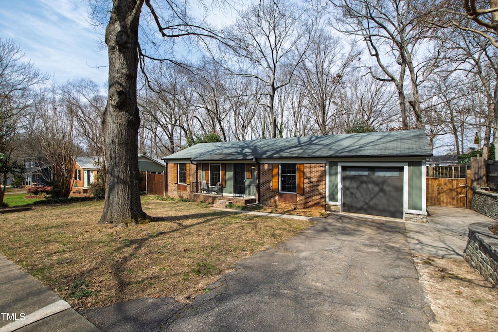 view of front facade with a garage, driveway, fence, a front lawn, and brick siding